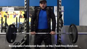 homme effectuant un shrug avec barre pour développer les trapèzes en salle de musculation