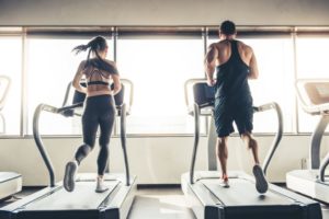 deux athlètes courant sur des tapis roulants dans une salle de sport bien éclairée