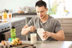 homme versant du lait dans un verre avec bananes et œufs pour mass gainer
