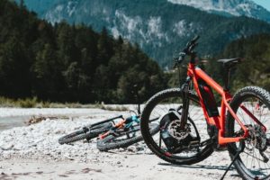 vélo électrique rouge vtt posé sur un chemin de montagne avec forêt en arrière-plan