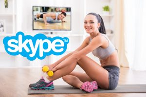 femme en tenue de sport avec haltères sur tapis de yoga devant écran montrant un coach skype