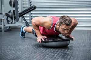 homme en planche sur bosu ball en salle de sport, exercice de gainage