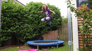 enfant qui saute sur un trampoline dans un jardin entouré de végétation