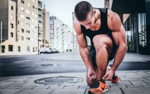 athlète musclé en tenue de sport ajuste ses chaussures de running en ville