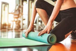 femme enroulant son tapis de yoga dans une salle de sport moderne