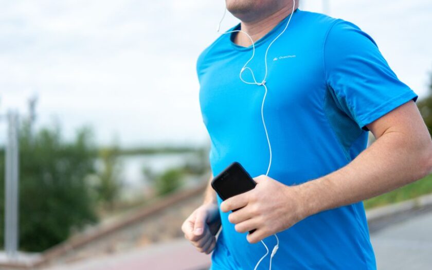 Close-up of a man jogging outdoors holding a smartphone wearing earphones.